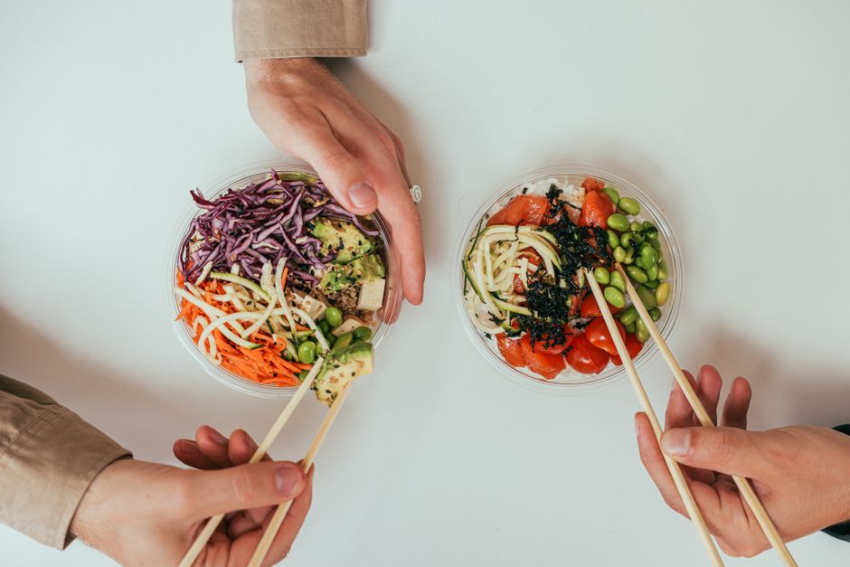 Top view of hands holding healthy vegetable salad bowls with chopsticks, featuring fresh ingredients.