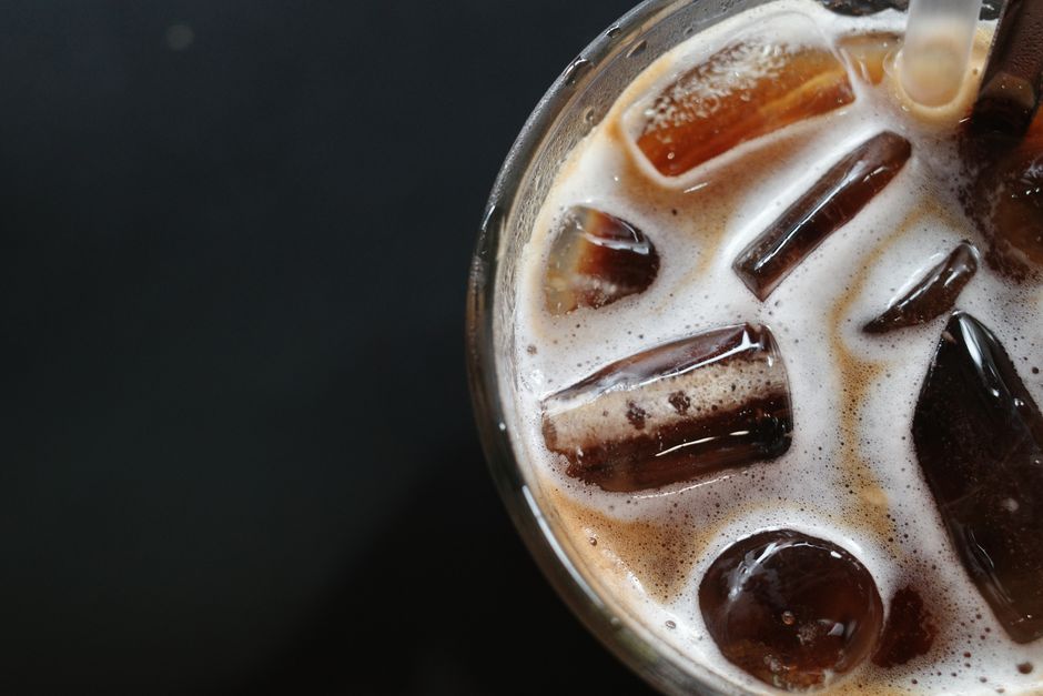 Top view of iced coffee with a straw, featuring ice cubes and frothy bubbles, against a black background.