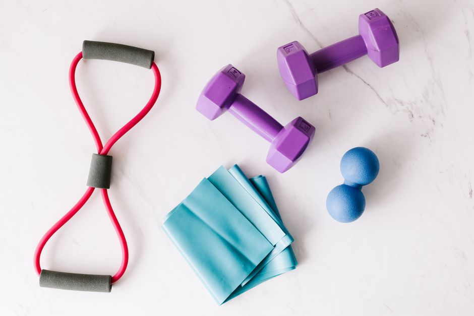 Top view of purple metal dumbbells and red tubular expander and blue tape expander and blue massage double ball placed on marble surface