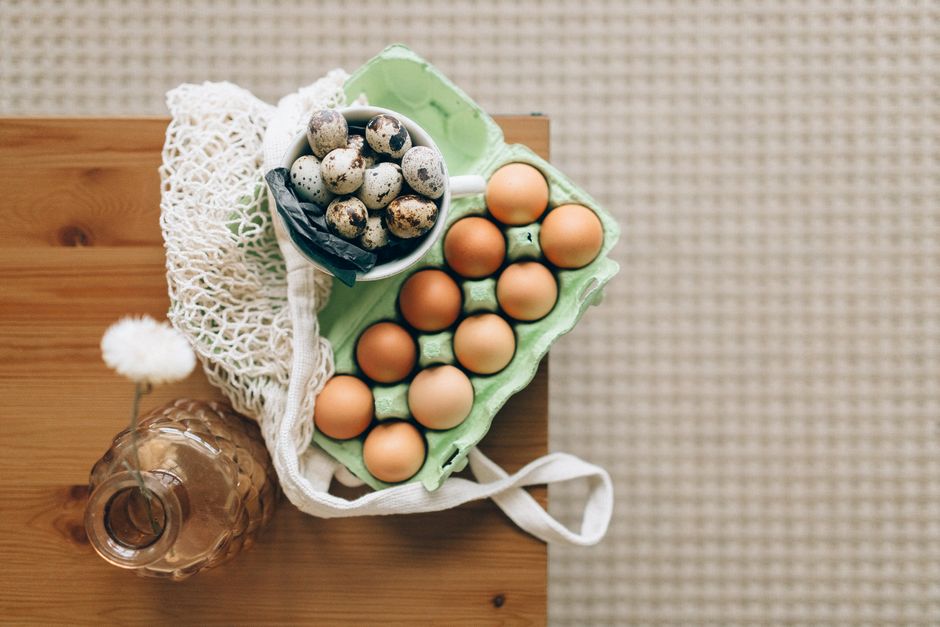 Top view of quail and chicken eggs in carton on a wooden table with organic produce vibe.