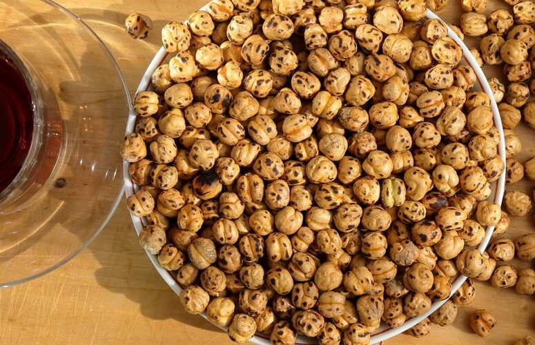 Top view of roasted chickpeas in a bowl and a red beverage on a wooden table.