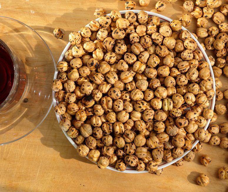 Top view of roasted chickpeas in a bowl and a red beverage on a wooden table.