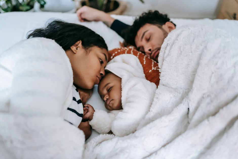 Tranquil ethnic couple sleeping with baby on comfortable bed in bedroom in apartment in daytime