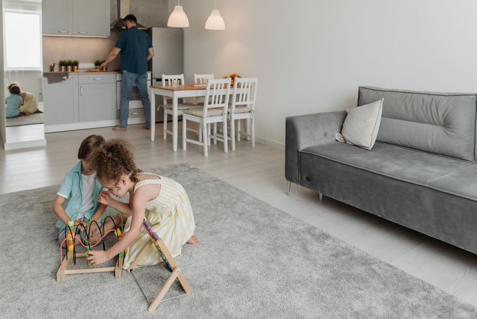 Two children playing on a rug as their father cooks in a modern, cozy home setting.