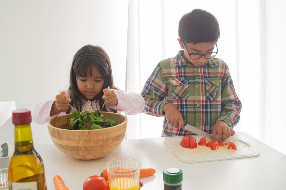 Two children prepare a healthy vegetable salad together at home, mixing ingredients with enthusiasm.