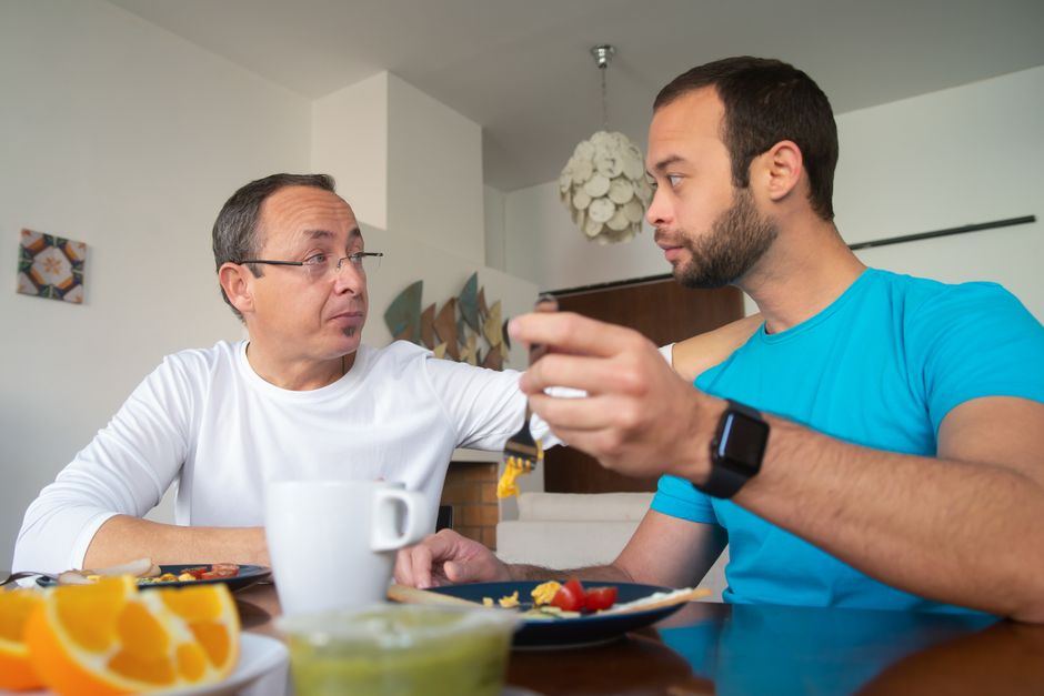 Two men enjoying breakfast together indoors, engaged in a warm conversation.