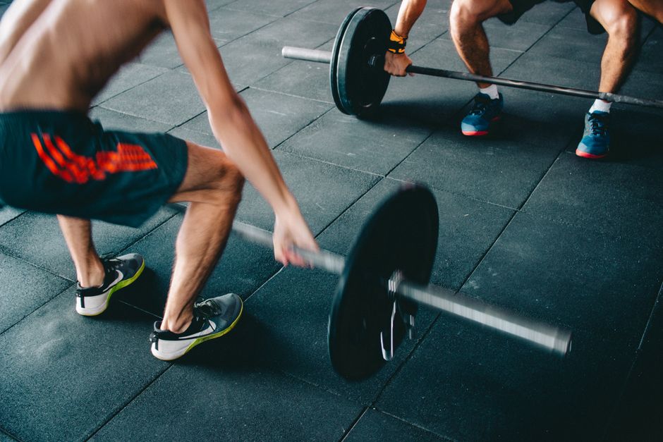 Two men lifting barbells showing strength and effort in a gym setting.