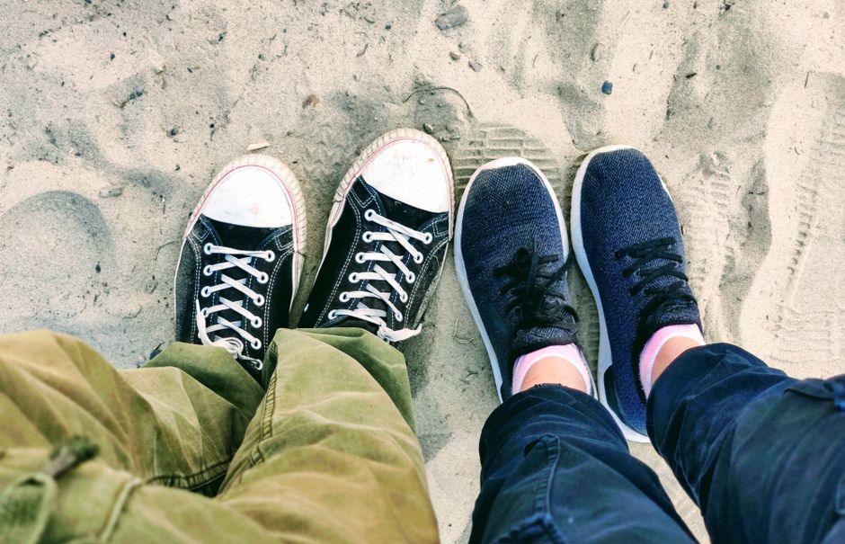 Two pairs of sneakers make footprints in the sand on a sunny day.