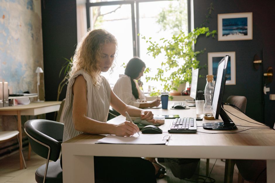 Two professional women focused on tasks in a bright, modern office, showcasing teamwork and productivity.