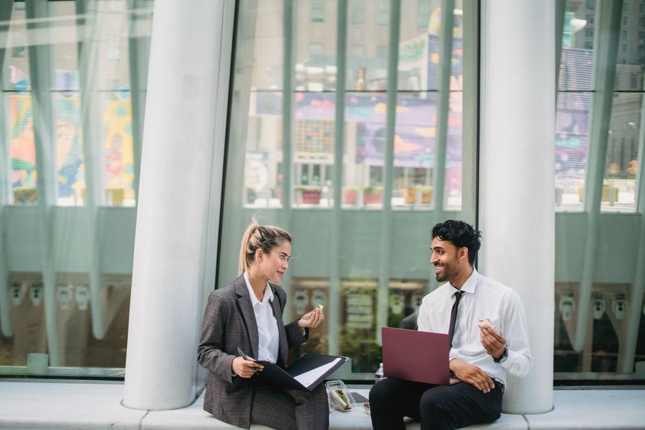 Two professionals share a casual snack meeting outdoors, enhancing work relationships.