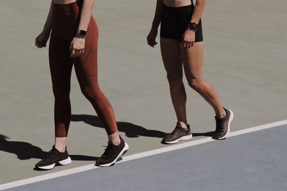 Two women exercise outdoors in leggings and sneakers, showcasing active lifestyle.