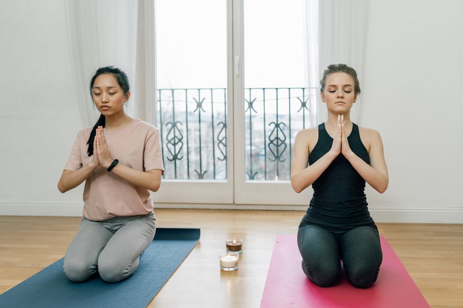 Two women meditating indoors on yoga mats, focusing on relaxation and mindfulness.