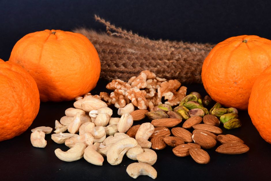Vibrant oranges paired with assorted nuts on a sleek black background, showcasing a healthy snack option.