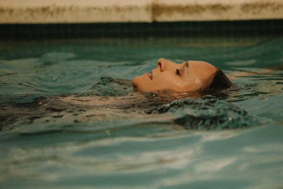 Woman peacefully floating in a calm pool, eyes closed, evoking relaxation and tranquility.