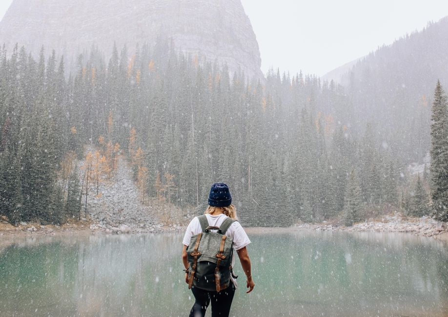 Woman with backpack enjoying a snowy day at the lake surrounded by pine trees.