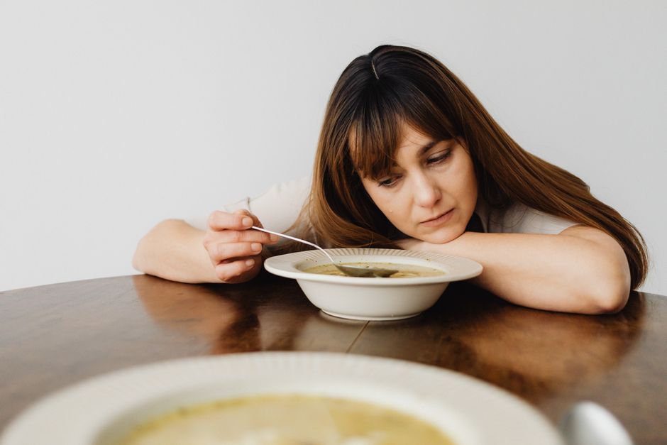 Woman with long hair looking bored while eating soup at a wooden table.