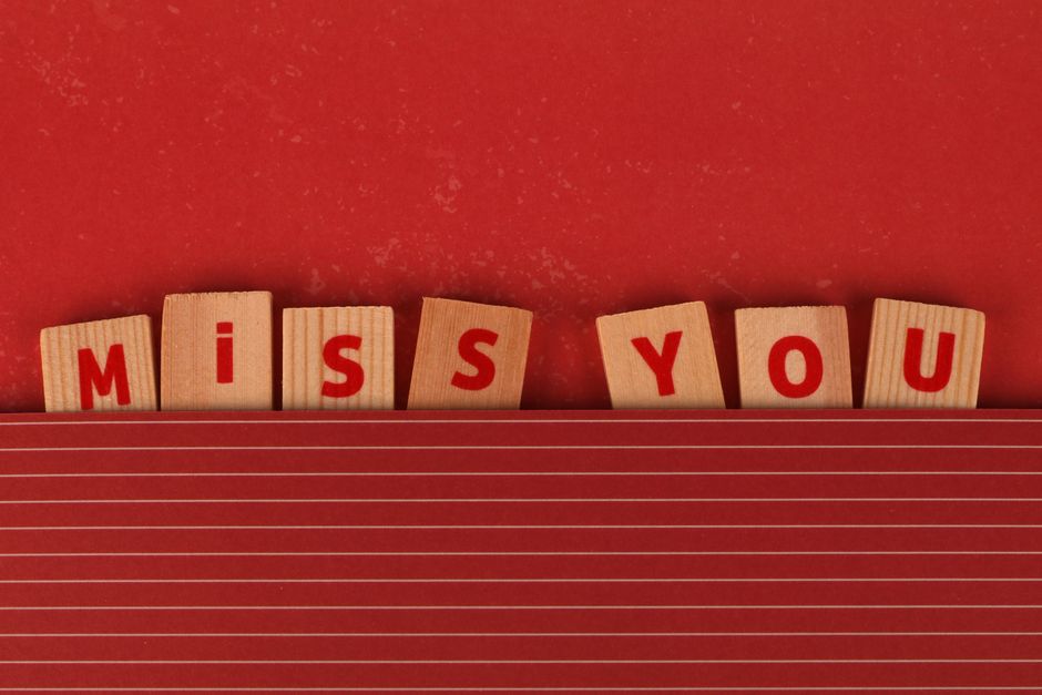 Wooden blocks with 'MISS YOU' text on a red background, expressing longing.
