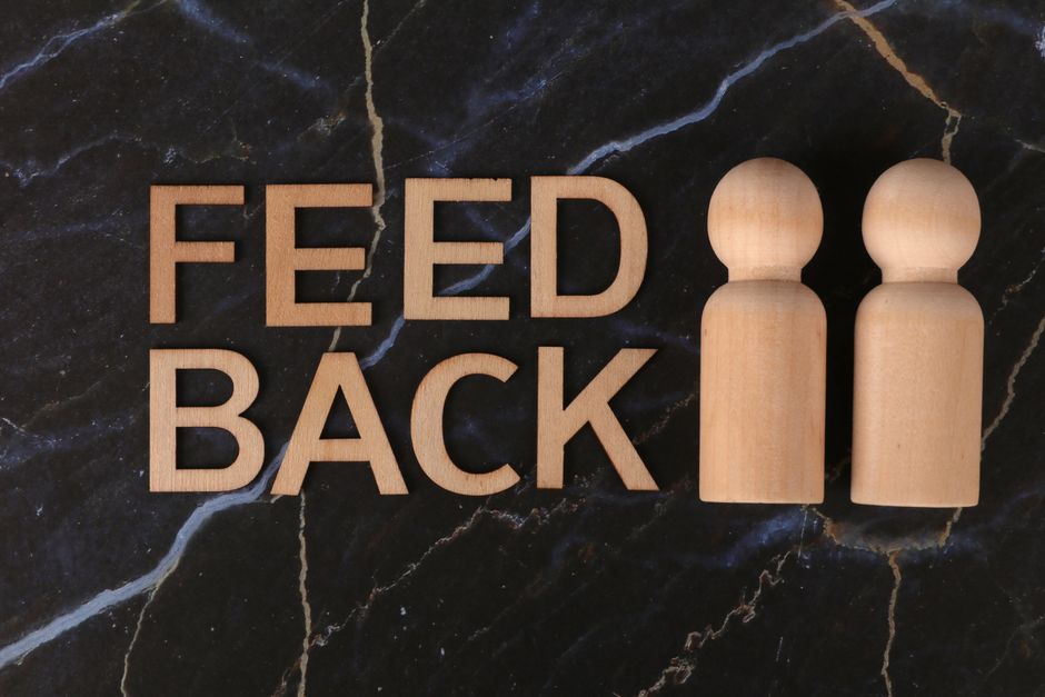 Wooden figures and 'feedback' text on black marble background, symbolizing communication and review.