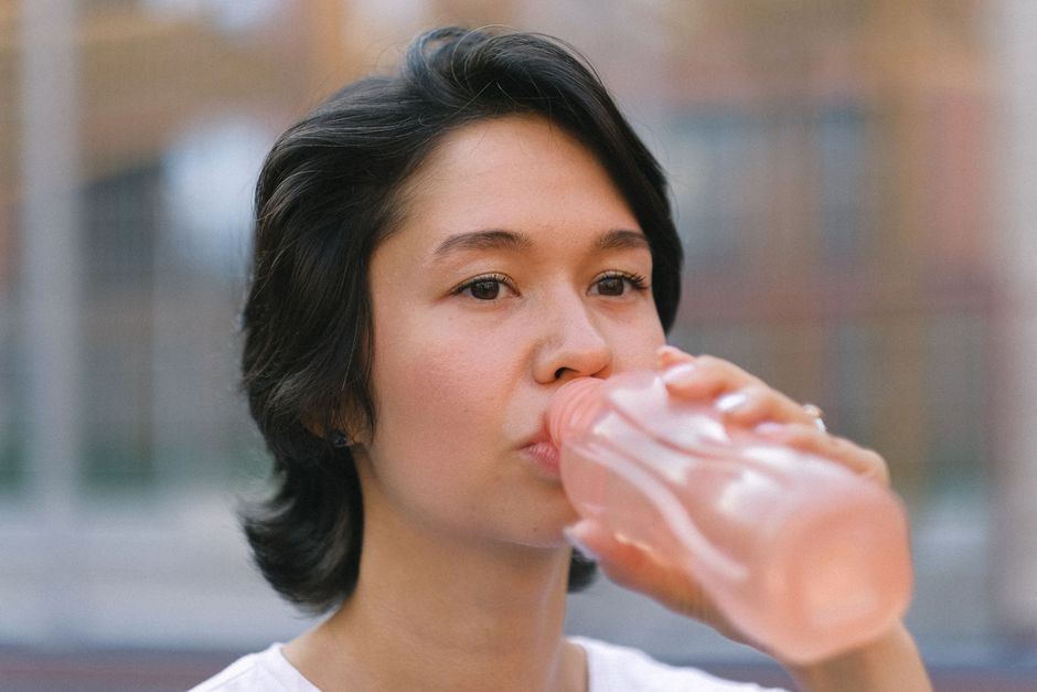 Young lady in activewear with bottle of water sitting on court near fence and looking away in day