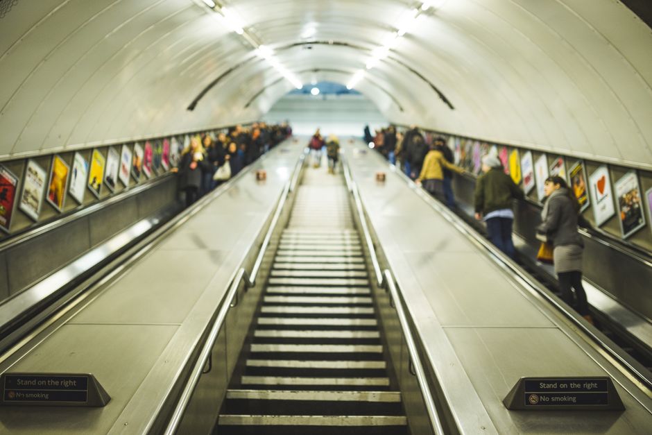 A bustling underground station showing commuters on escalators with signs and advertisements.