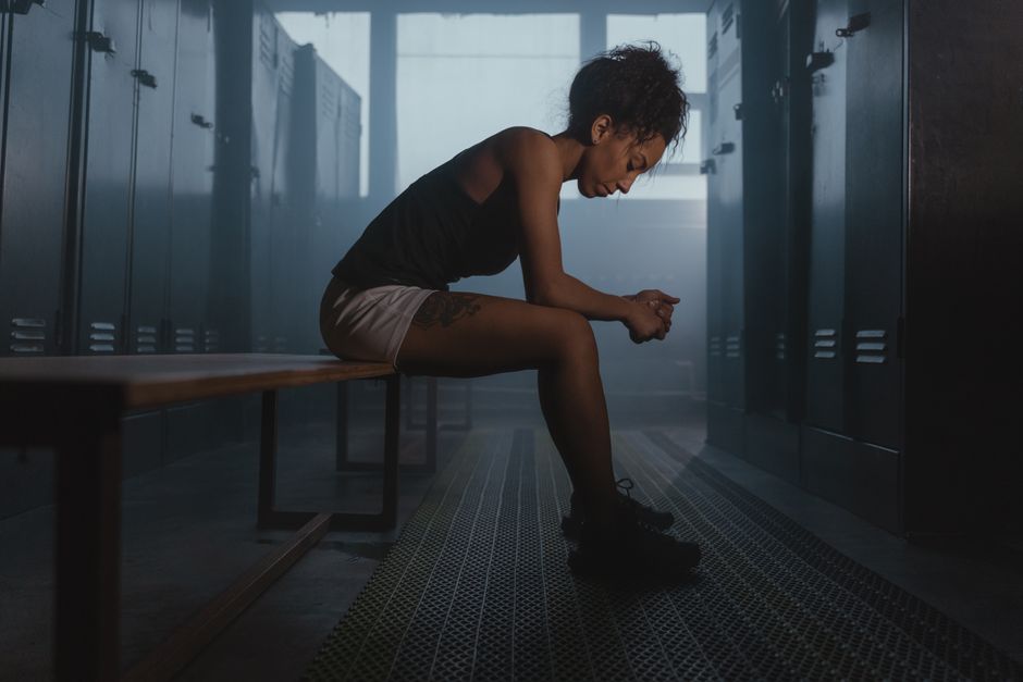 A contemplative athlete sits in a dimly lit locker room, embodying strength and introspection.
