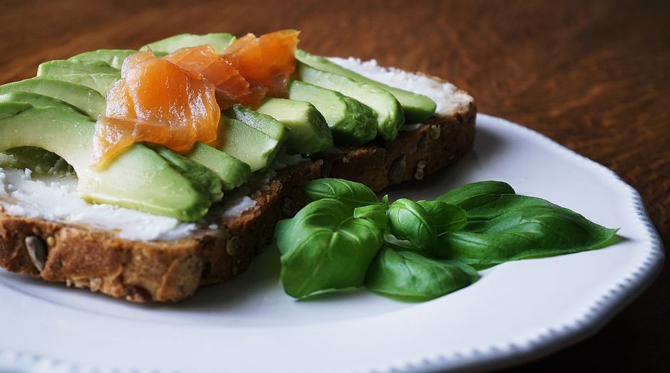 A delicious, healthy meal with avocado and smoked salmon on seeded bread, garnished with basil leaves.