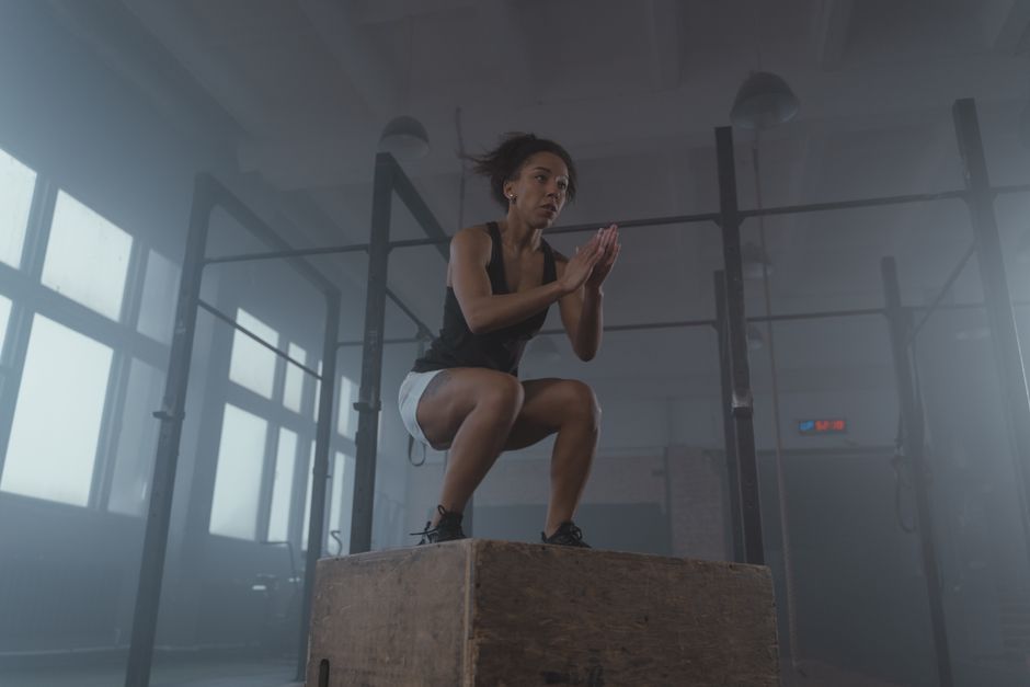 A determined woman executing a box jump in an indoor gym setting, showcasing strength and fitness.