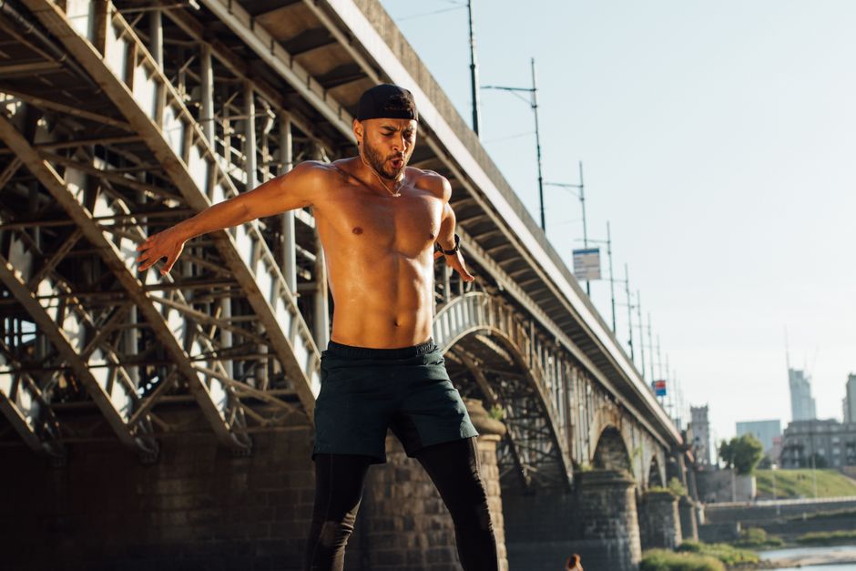 A fit man engages in an enthusiastic outdoor workout under a city bridge during the day.