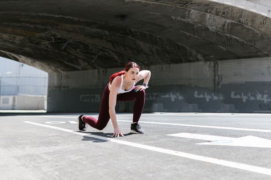 A focused female athlete in sportswear ready to sprint outdoors in an urban setting.