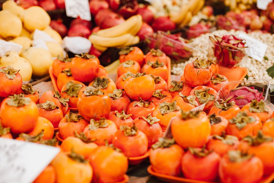 A lively display of ripe persimmons surrounded by various fruits in an outdoor market setting.