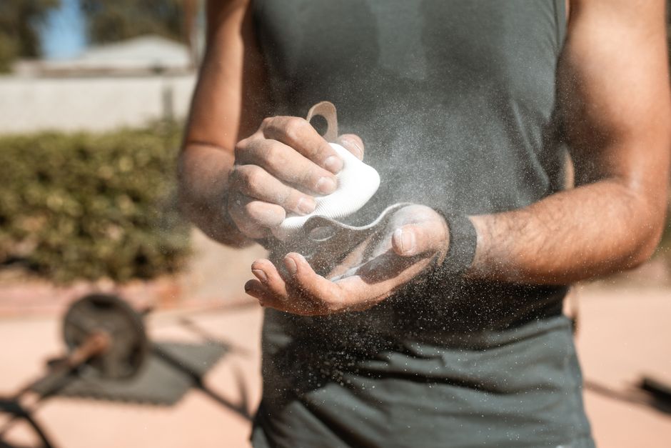 A man applies chalk to his hands during an outdoor weightlifting session, emphasizing fitness.