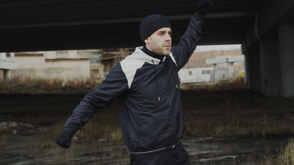 A man exercises under a bridge, wearing warm athletic clothing.