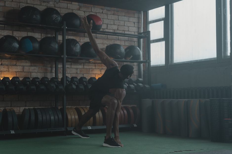 A man performing dynamic stretching exercises in a gym setting with fitness equipment in the background.