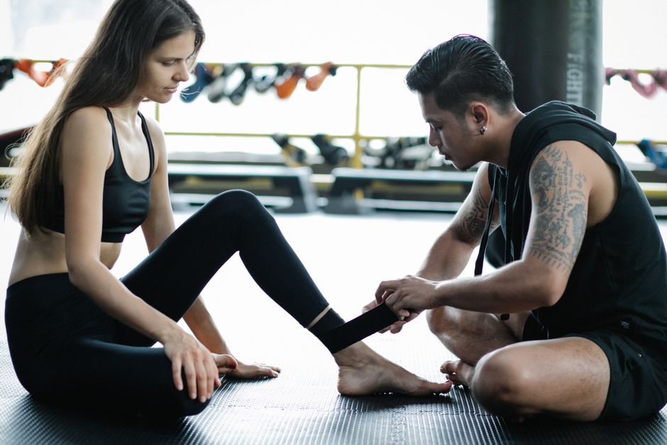 A man tapes a woman's ankle in a modern gym setting, focusing on preparation and support.