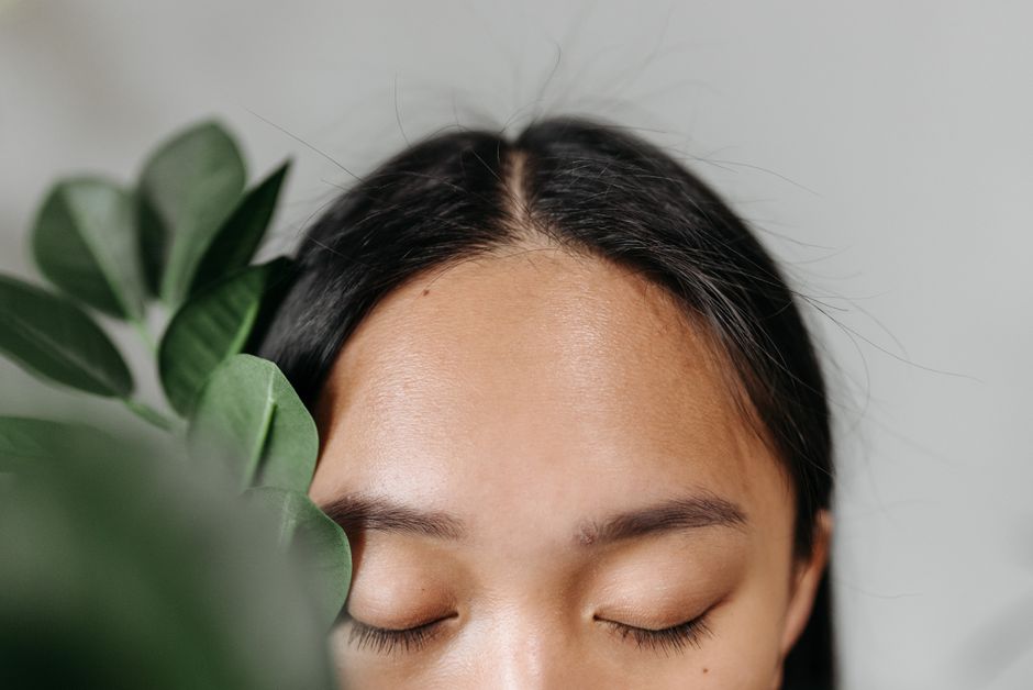 A peaceful portrait of a woman with closed eyes surrounded by lush green leaves. Perfect for wellness themes.
