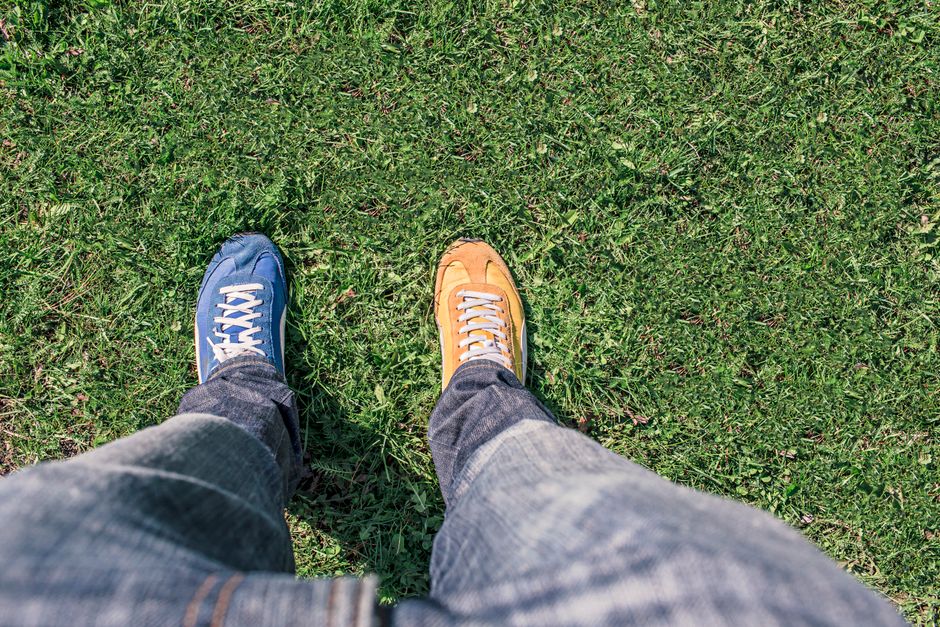 A person wearing mismatched shoes stands on green grass, highlighting differences and individuality.