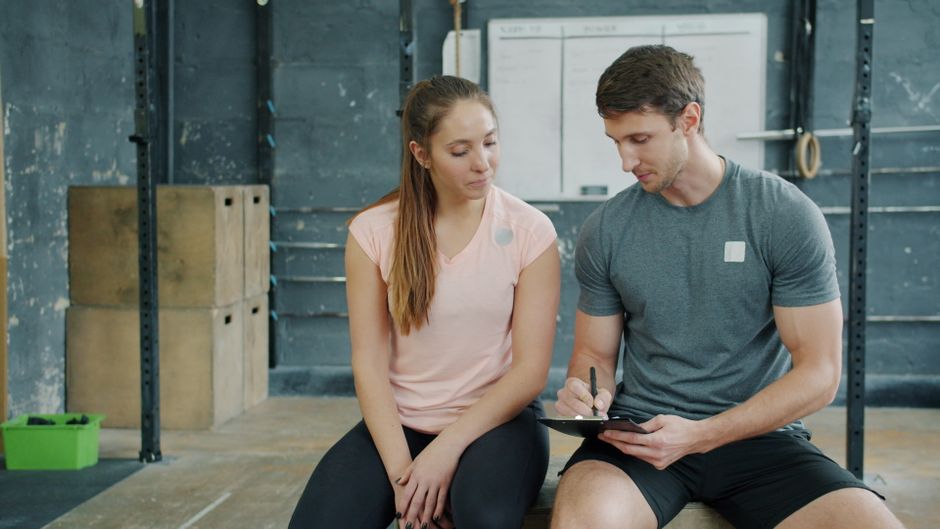 A personal trainer and client reviewing a fitness plan together inside a gym.