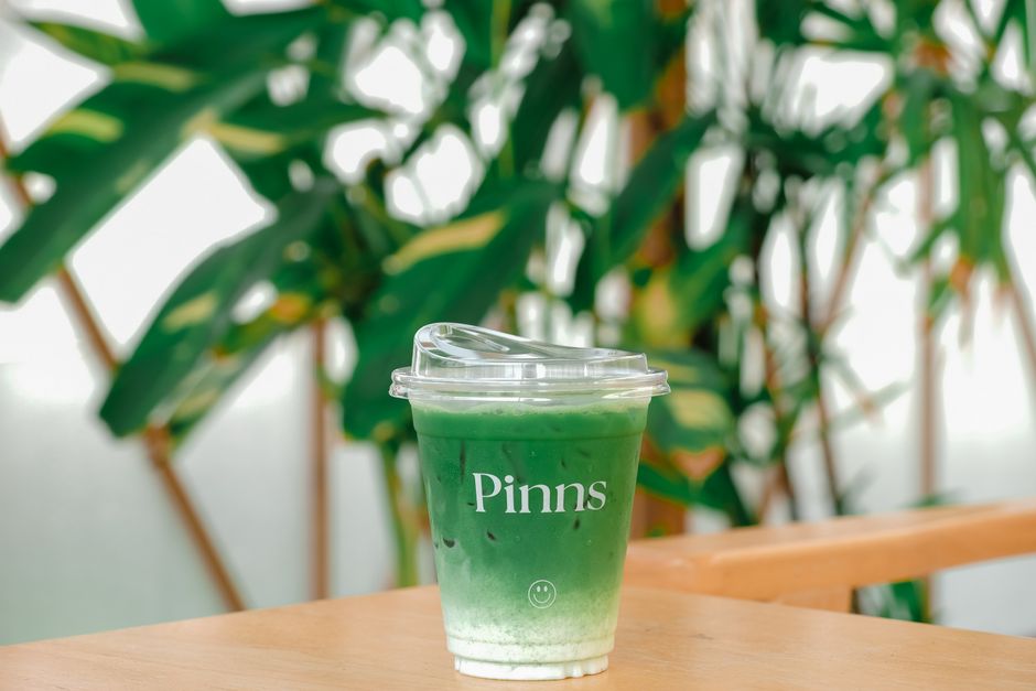 A refreshing iced matcha latte in a plastic cup on a wooden table with green leaves in the background.