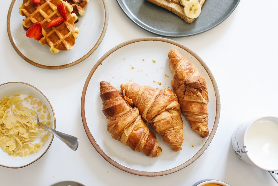 A tempting breakfast spread with croissants, waffles with strawberries, and cereal in a flatlay setting.