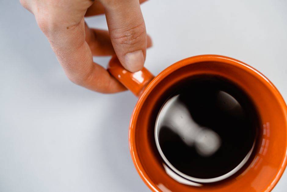 A top view of a hand holding an orange cup filled with coffee.