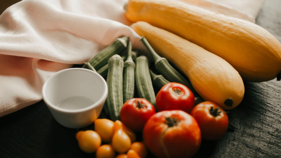 A variety of fresh vegetables including yellow squash, okra, and tomatoes on a rustic table setting.