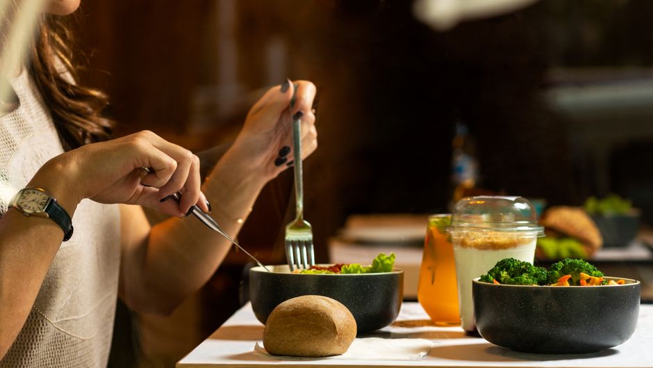 A woman dining on a fresh salad with vegetables and a drink indoors.
