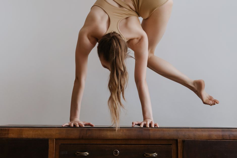 A woman elegantly balances in a handstand on a wooden table, showcasing flexibility and strength.