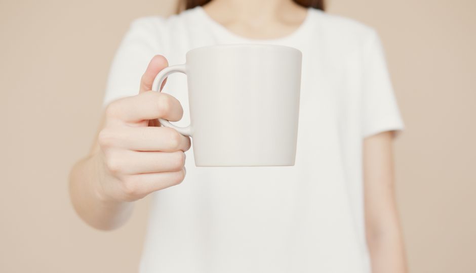 A woman holding a plain white mug, perfect for branding or mockup uses.