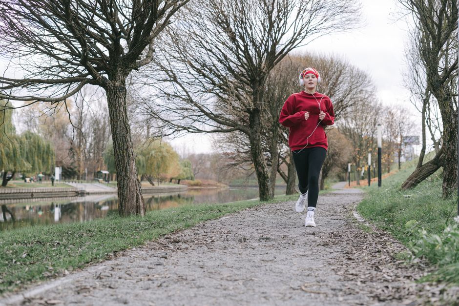 A woman in a red outfit jogs along a tree-lined path by a calm river, capturing an autumn fitness vibe.