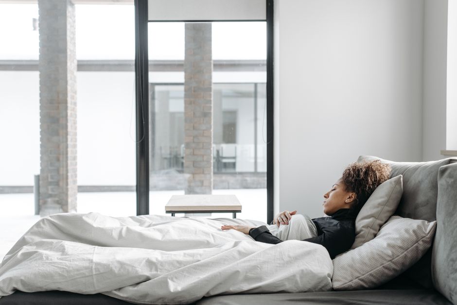 A woman rests comfortably in bed in a bright, minimalistic room.