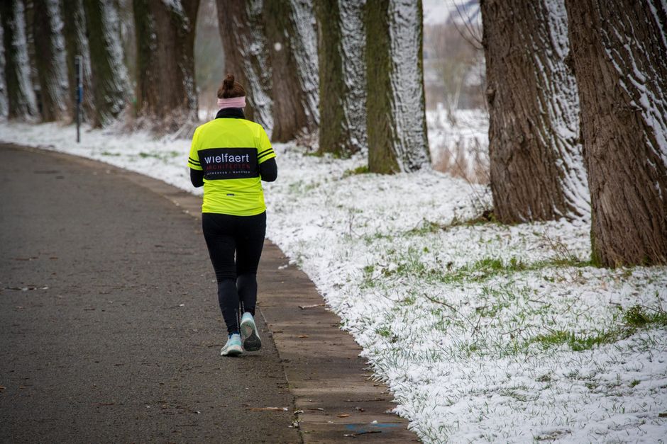 A woman walks down a snow-lined path in winter, wearing bright running gear.