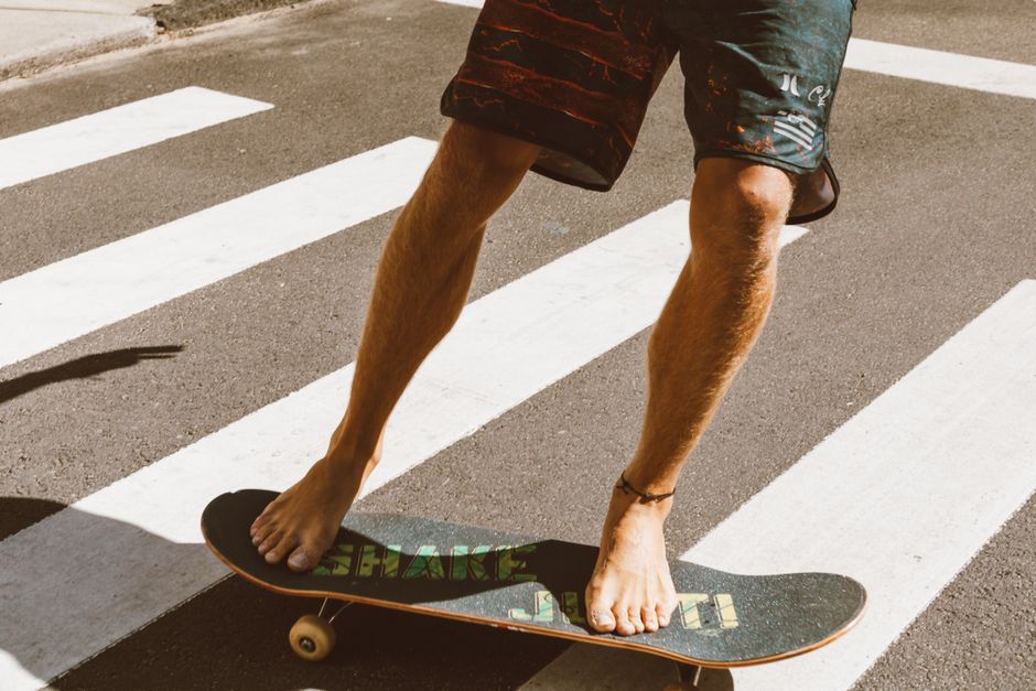 A young adult skateboards barefoot across a sunlit pedestrian crossing, showcasing balance and motion.