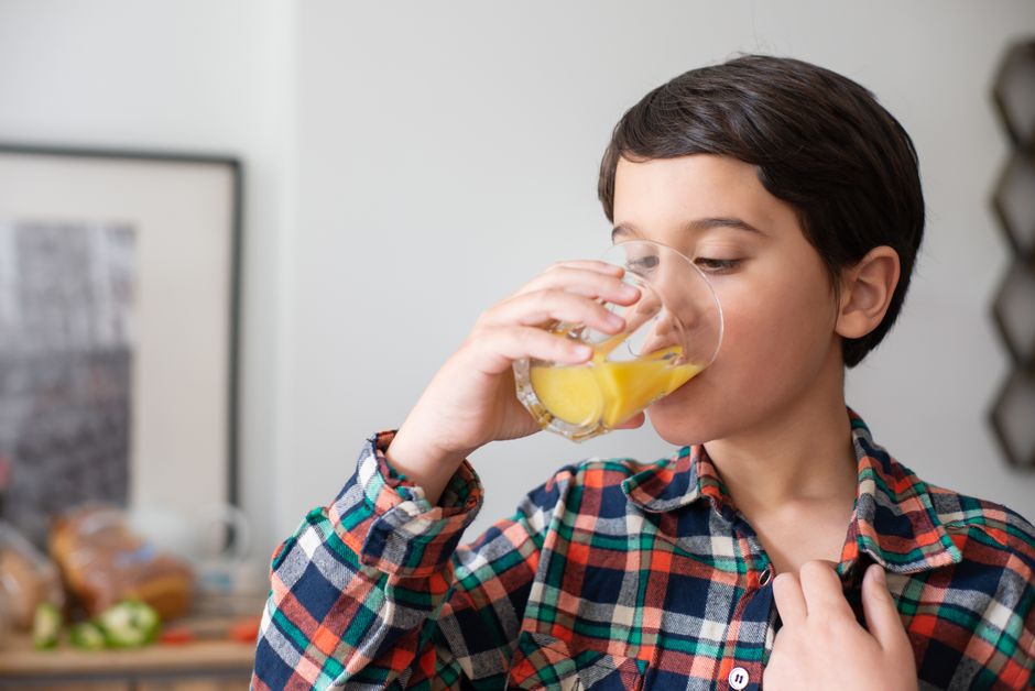 A young boy drinks fresh orange juice in a cozy indoor setting, wearing a colorful plaid shirt.