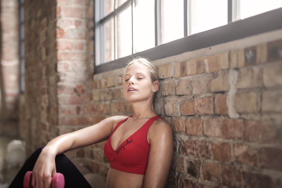 A young woman in activewear rests against a brick wall after exercising, showcasing fitness and dedication.